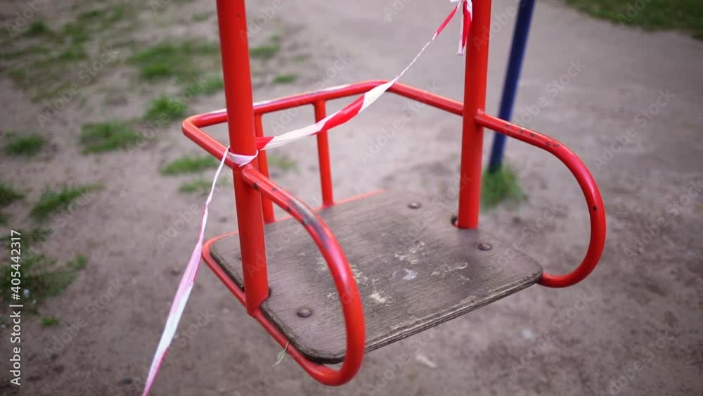 Empty children public playground. Seat of swing closed with warning signal red and white ribbon because of lockdown measures in public places. Restriction and caution of pandemic Covid-19 concept Empty children public playground. Seat of swing closed with warning signal red and white ribbon because of lockdown measures in public places. Restriction and caution of pandemic Covid-19 concept