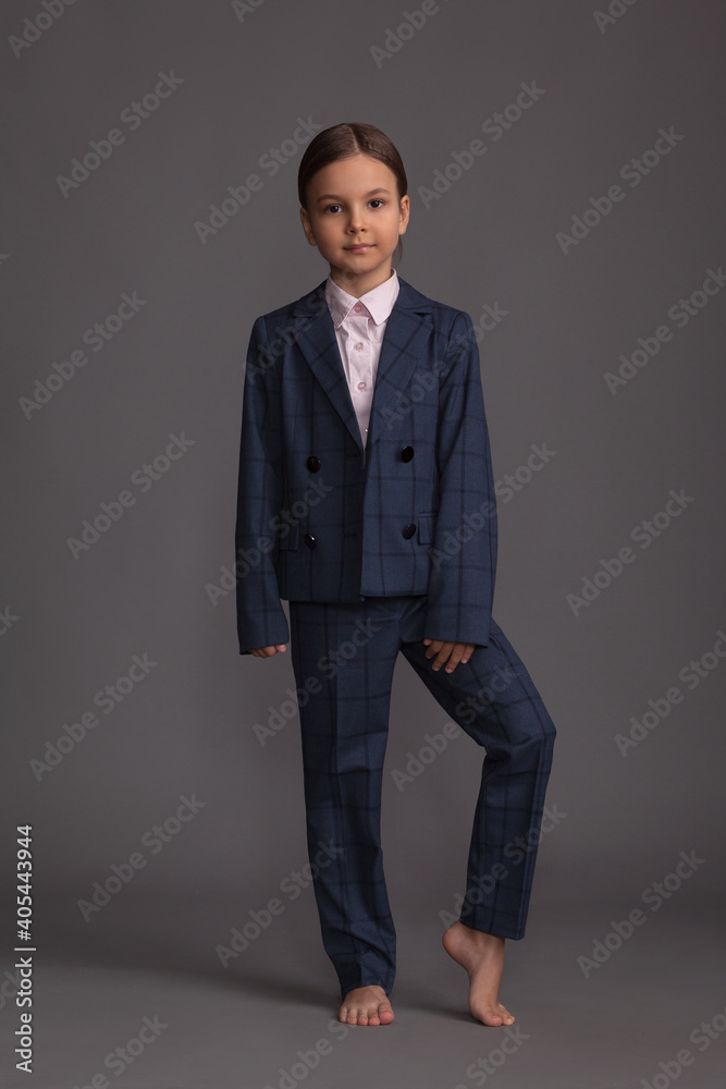 Beautiful little girl in a pink shirt with a stylish plaid trouser suit posing in the studio on a gray background barefoot Beautiful little girl in a pink shirt with a stylish plaid trouser suit posing in the studio on a gray background barefoot