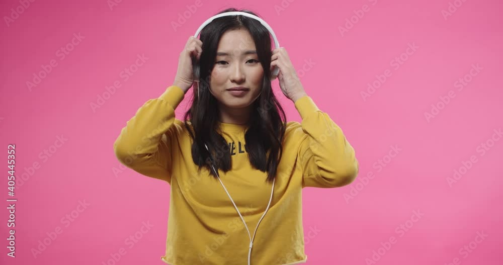 Portrait of Asian young beautiful joyful woman in yellow blouse standing isolated over pink wall background, putting on white headphones and listens to music or favorite songs. Leisure concept Portrait of Asian young beautiful joyful woman in yellow blouse standing isolated over pink wall background, putting on white headphones and listens to music or favorite songs. Leisure concept