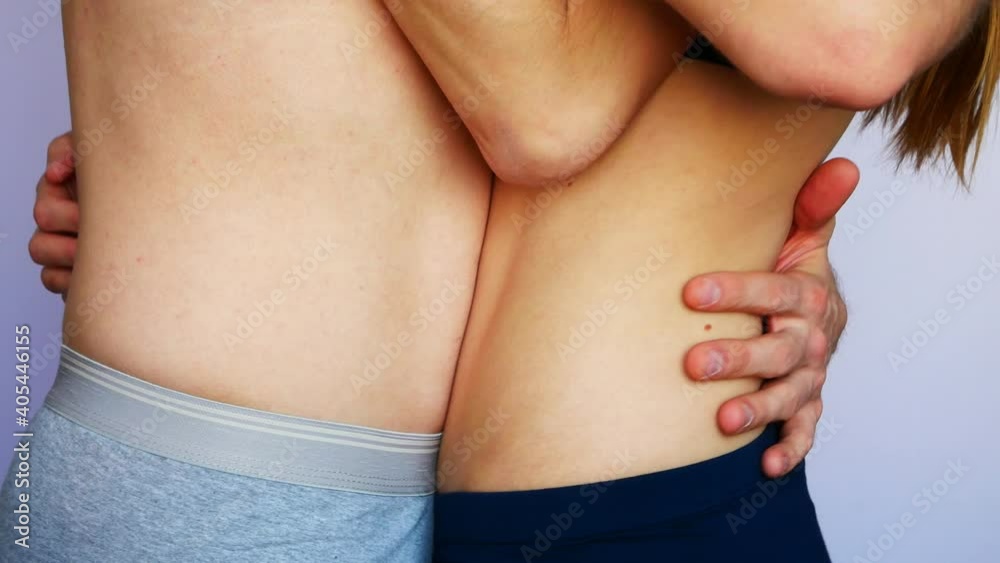 Close-up of the waists of hugging young man and woman topless against white background
