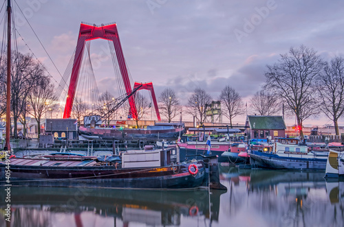 Rotterdam, The Netherlands, January 13, 2021: theOld Harbour with istoric barges and the illuminated red pylons of Willems Bridge just before sunrise photo