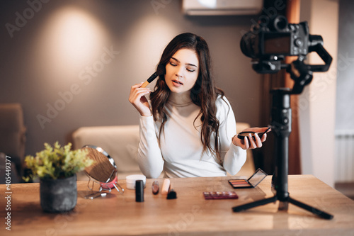 Beauty blogger nice female filming daily make-up routine tutorial on camera. Influencer young woman live streaming cosmetics product review in home studio. Vlogger job. DIY putting makeup