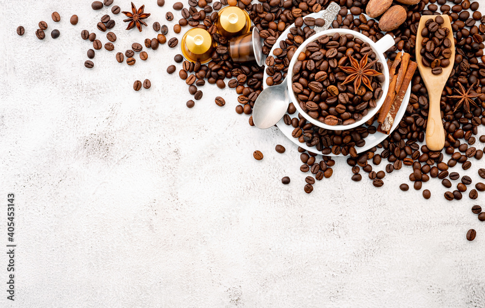 Background of dark roasted coffee beans and capsules with scoops setup on white concrete background with copy space. Background of dark roasted coffee beans and capsules with scoops setup on white concrete background with copy space.