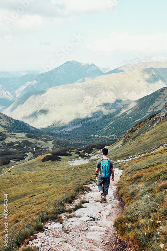 Young man with backpack hiking in a mountains, actively spending summer vacation. Rear view of teenager walking up on a hill along mountain path © Przemek Klos