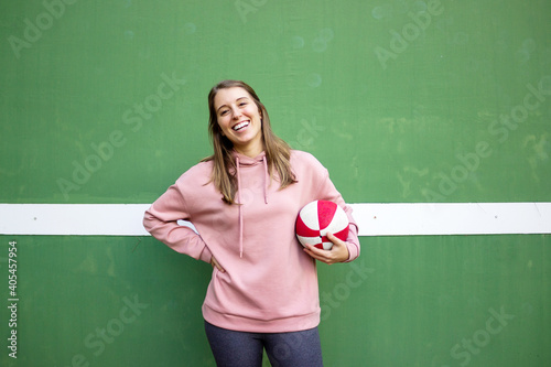 young long haired woman holding a basket ball against green wall