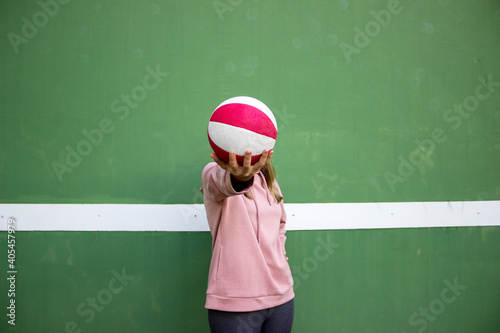 young long haired woman holding a basket ball against green wall © 2Design
