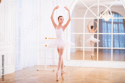 young ballerina standing on pointe in a tutu in beautiful white hall in front of the mirror.