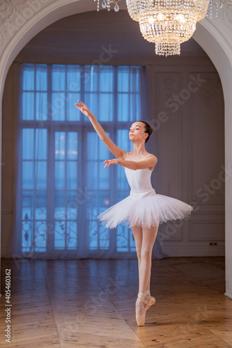 young slender ballerina in white tutu dances on pointe shoes in a spacious, bright room with large windows. photo