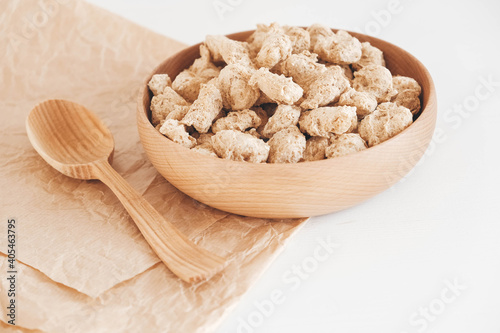 Raw dehydrated soy meat or dry soya chunks in wooden plate with a wooden spoon on white background. Top view. Copy, empty space for text