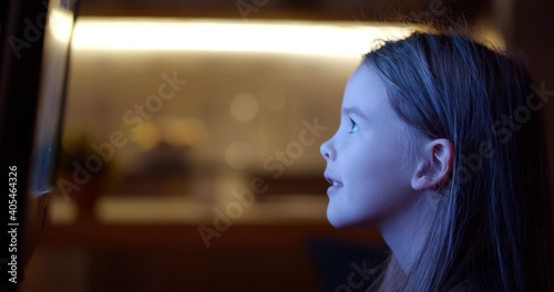 Bilde på lerret Side view of little girl sitting neat tv screen and watching cartoons