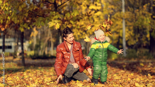 Mom and son throw autumn leaves in autumn park, family fun. family enjoying a walk in nature. happy motherhood concept.