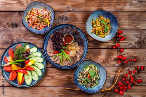 Flat layout of various dishes with sliced vegetables  meat cuts  salads on a brown wooden background.