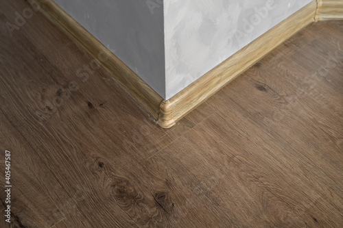 Laminate with plastic baseboard with a wooden texture. Newly installed wooden laminate flooring and baseboards in home. Modern design. Close up of plastic plinths on dark wooden oak floor parquet.
