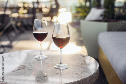 Two glasses of red wine on a sunny fancy restaurant terrace. Marble tables, cosy couch, sunset light, rooftop 