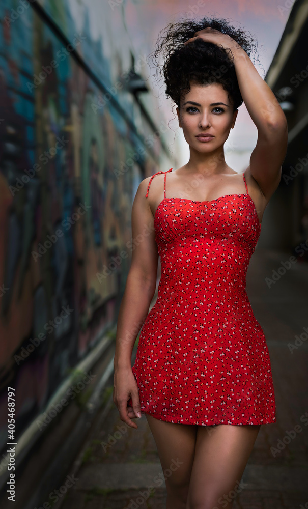 A beautiful young curly-hair woman in a little red dress is walking on the street. - Portrait Photography. 