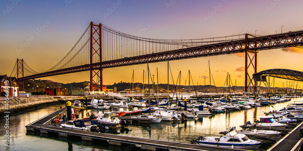 Barcas amarradas en el puerto bajo el Puente colgante 25 de abril sobre el tajo en Lisboa al atardecer