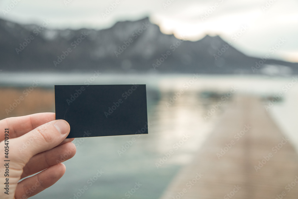 blank business card for your text and logo on the background of the Austrian mountain lake. black blank business card. black sheet of cardboard in hand and free standing blank business card for your text and logo on the background of the Austrian mountain lake. black blank business card. black sheet of cardboard in hand and free standing
