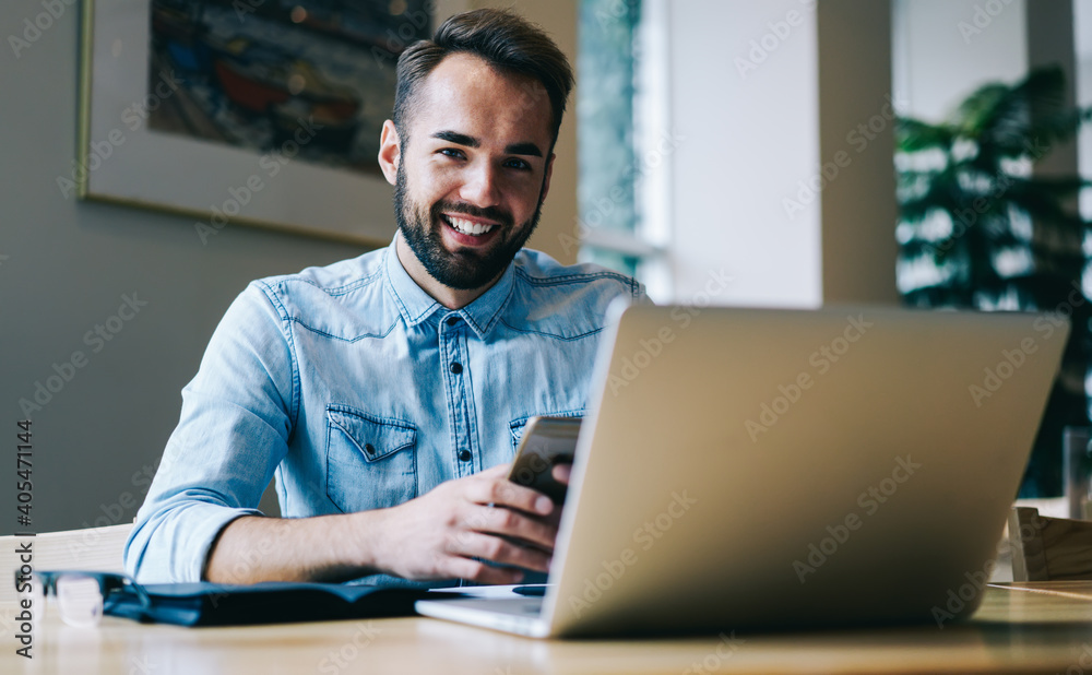 Smiling freelancer using smartphone while working on laptop Smiling freelancer using smartphone while working on laptop