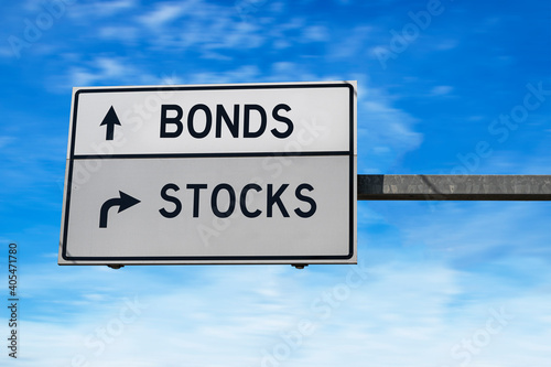 Road sign with words bonds and stocks. White two street signs with arrow on metal pole on blue sky background.