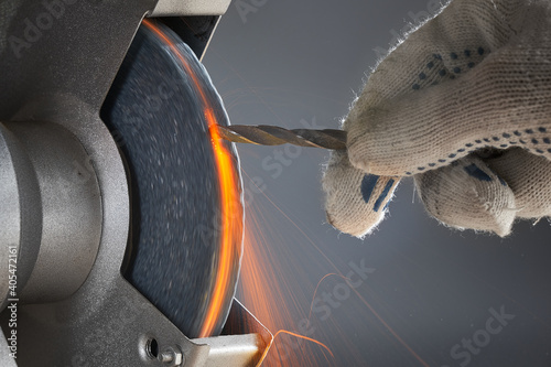 Tableau sur toile The hand wearing a work glove of man regrinding the drill tool for sharpen the drill tool with grinding wheel