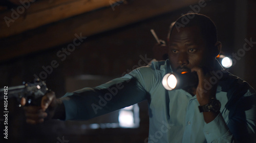Foto Afro-american detective and his partner with gun and flashlight investigating da