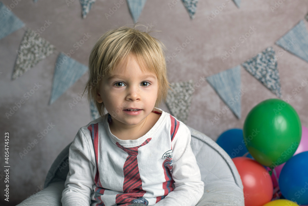 Fototapeta premium Cute blond toddler child, boy, sitting on little baby armchair, playing with colorful balloons