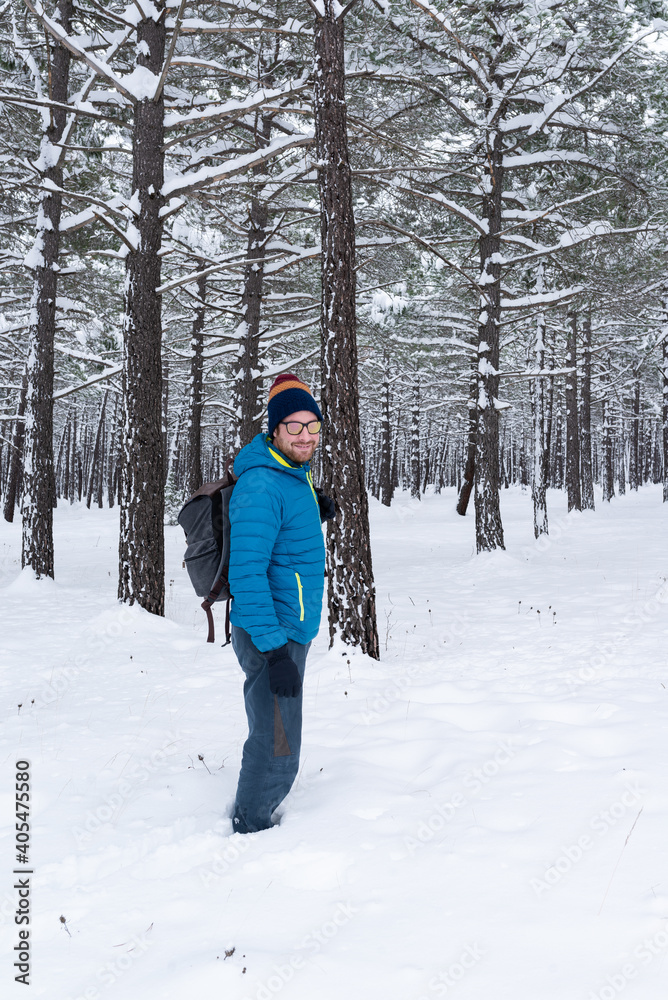 Handsome bearded caucasian man standing in a snowy pine forest. Winter outdoor activities.
