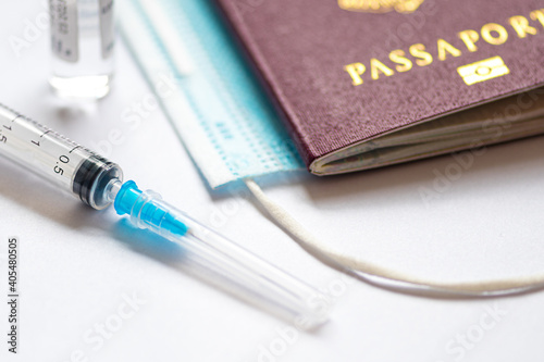 Syringe with needle, vial, surgical face mask and passport or visa on a white table ready to be used. Covid or Coronavirus vaccine 