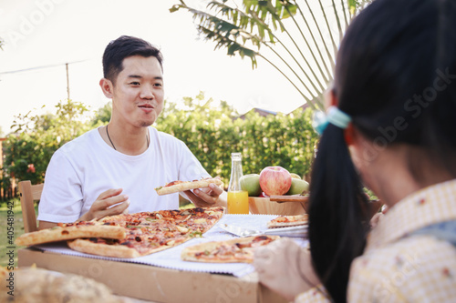 Happy asian family having enjoying meal(pizaa, salad,snack, orange juice) together in home garden. Outdoor dinner party in holiday. Multi generation family concept.