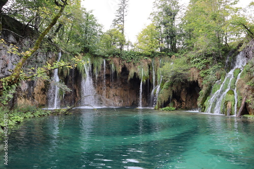 Fototapeta Naklejka Na Ścianę i Meble -  Scenic view of a lake overgrown with green trees with emerald turquoise clear water, and a waterfall with powerful jets of water, autumn at Plitvice Lakes National Park 
