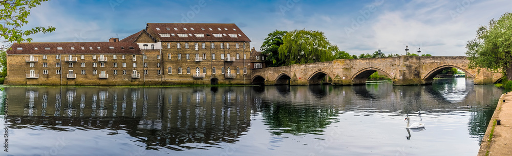 A panorama view of the mill and old bridge at Riverside, Godmanchester reflected in the calm waters of the River Great Ouse in springtime