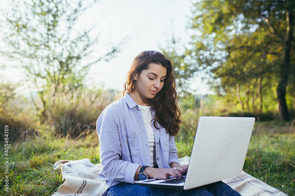 Beautiful woman, resting sitting onthe grass, and using a laptop Beautiful woman, resting sitting onthe grass, and using a laptop
