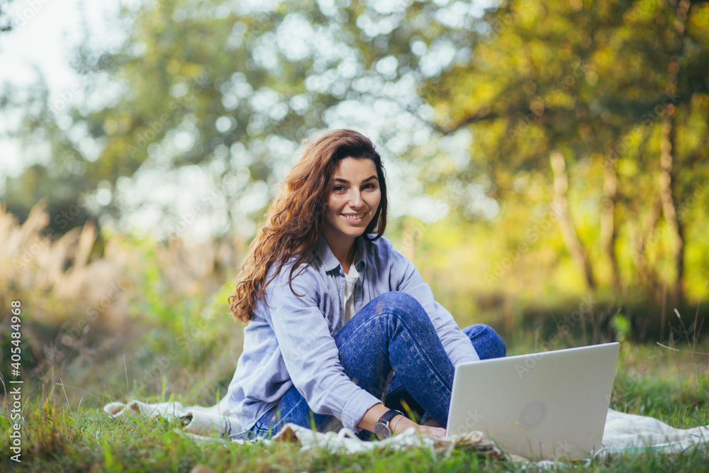 Beautiful woman, resting sitting onthe grass, and using a laptop Beautiful woman, resting sitting onthe grass, and using a laptop