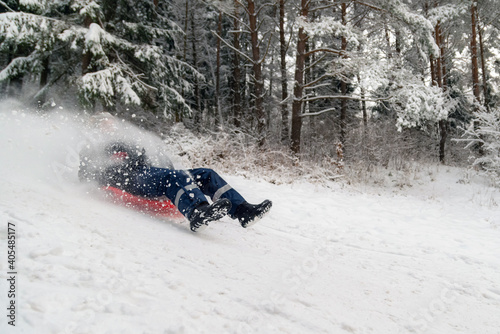 Person with a sled going fast down the white snowy hill in the forest. Seasonal winter happiness.