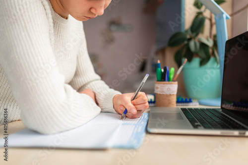 Beautiful schoolgirl studying at home doing school homework. Distance learning online education © len44ik