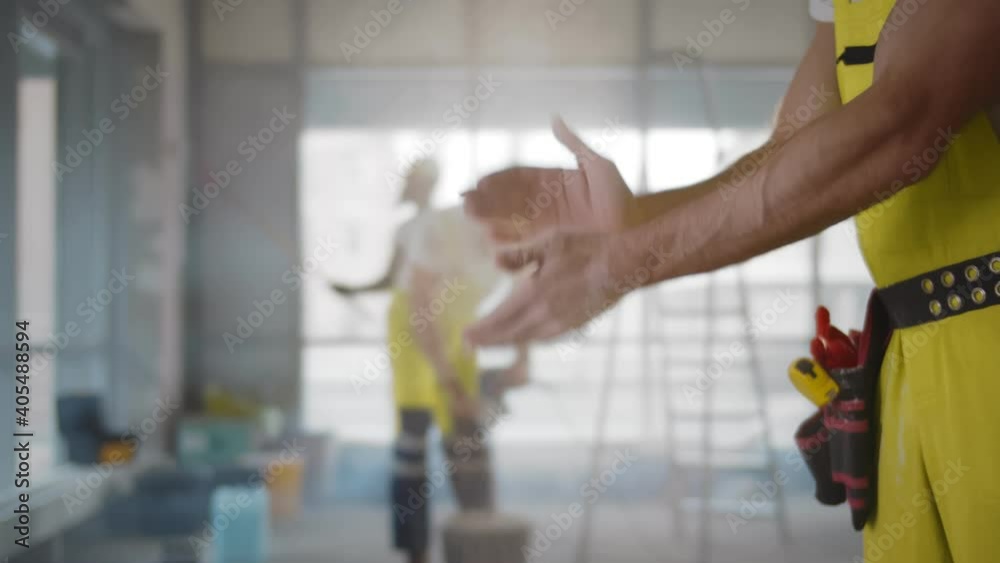 Close up of builder in uniform shaking off hands redecorating apartment Close up of builder in uniform shaking off hands redecorating apartment