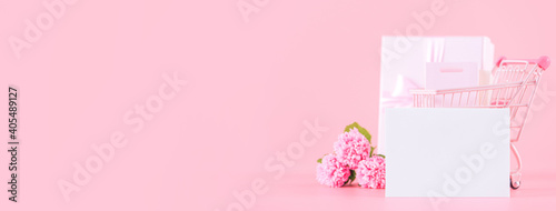 Shopping cart and gift with carnation on pink table background. © RomixImage