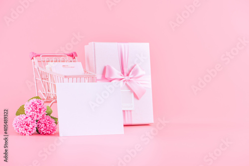 Shopping cart and gift with carnation on pink table background. © RomixImage