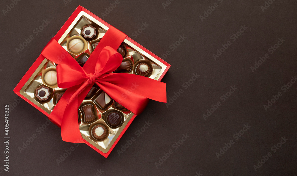 Box of chocolate pralines with red bow on dark brown background. Image with copy space