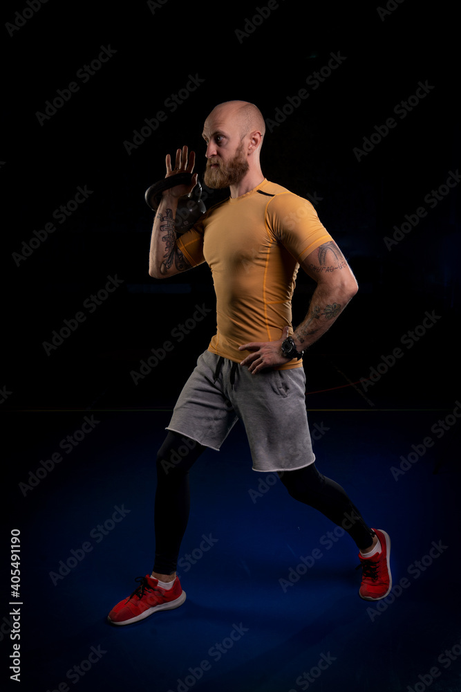 bearded athlete with tattoos preparing to lift a kettlebell with one hand