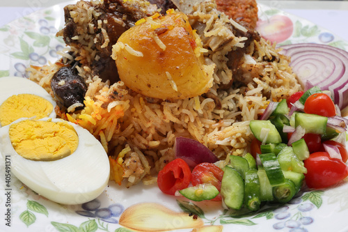 Home style mutton kacchi biryani with potato chop tomato cucumber onion salad on old style plate photo