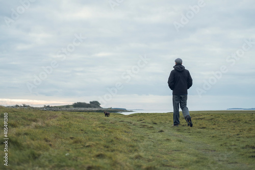 A young man walking and contemplating life by the quiet sea and mountains, surrounded by raw concrete sea defence wall. Mental health and depression road to recovery.