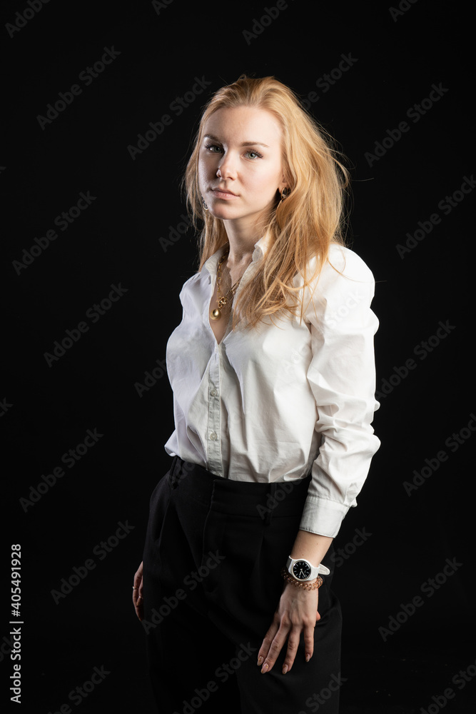 youth stands on a black background in a white blouse. Smiling smiling at camera, urban life concept, in studio, business woman, blonde youth stands on a black background in a white blouse. Smiling smiling at camera, urban life concept, in studio, business woman, blonde