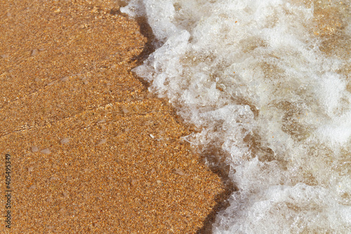 Fényképezés A sea wave with white foam runs over the yellow sand of the seashore