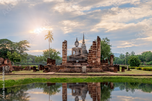Buddha statue and pagoda Wat Mahathat temple with reflection during sun set, Sukhothai Historical Park, Thailand © wirojsid
