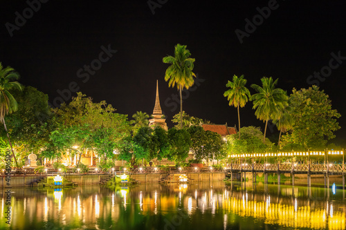 Pagoda and monastery complex Wat Traphang Thong temple during night with wooden bridge and reflection, Sukhothai, Thailand photo