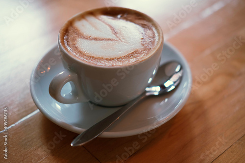 A beautiful creamy brown warm fresh cappuccino coffee cup, full of creamy coffee, served in a wooden rustic brown coffee shop with coffee art. Organic fair trade coffee photographed fromabove