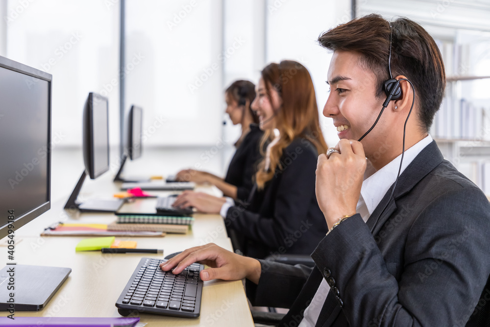 Young Asian male customer service support agent operator team working in call center office with headsets and computer. Young Asian male customer service support agent operator team working in call center office with headsets and computer.