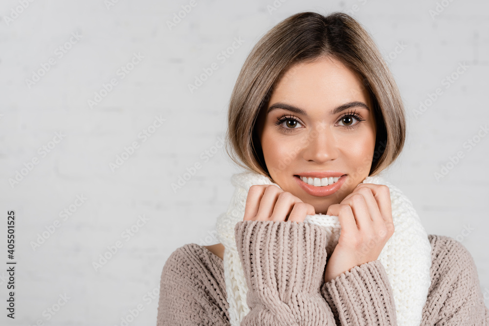 Young woman in sweater smiling at camera while holding scarf on white background Young woman in sweater smiling at camera while holding scarf on white background