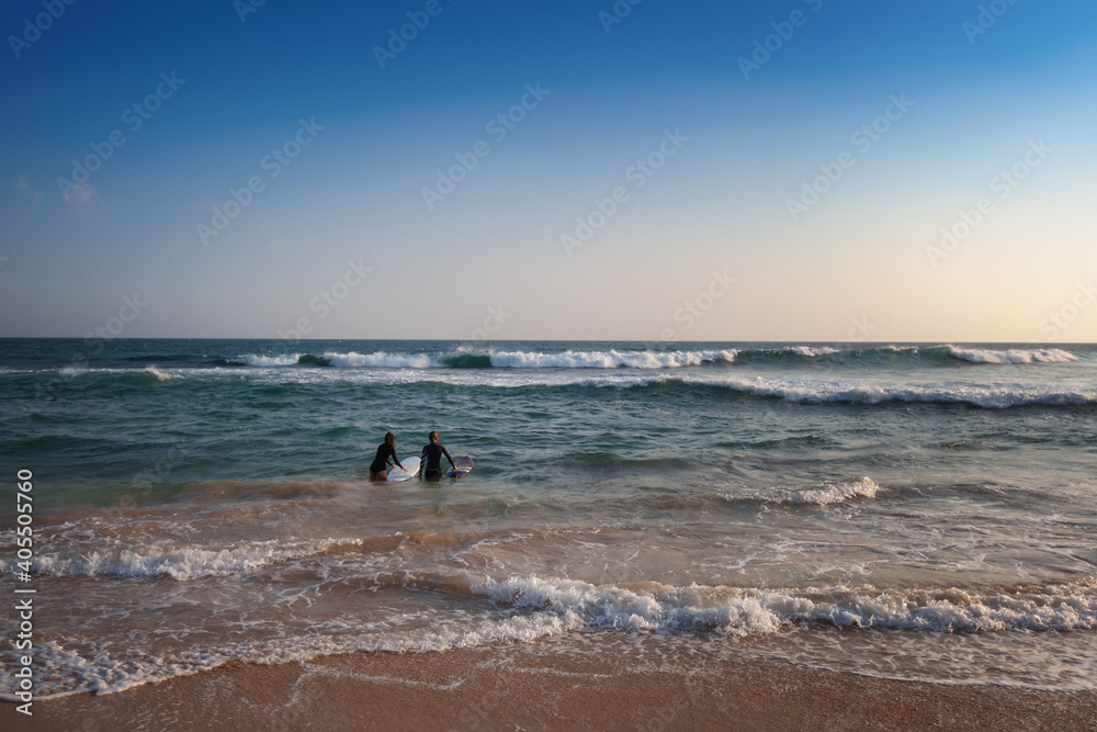Young couple going into ocean waves with surfboards on beautiful tropical beach